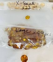 Bag of 22 extra small amber-colored glass pieces and bag of 49 large amber-colored glass pieces with one large piece displayed outside.