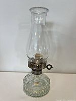 Front view of clear glass oil lamp with embossed base and tall chimney