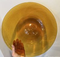 Top view of large amber serving platter held up by hand to show size and bubble details.