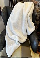 Cream-colored faux fur side of the throw blanket draped on a black leather chair