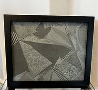Frontal view of one framed abstract art piece, a metal engraved printing plate with geometric and floral etching, in a black frame