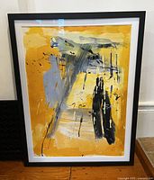 Front view of the original framed abstract painting showing yellow-orange background with black, gray, and white brush strokes and splatters.