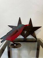 Plasma cut handpainted bird with two metal stars behind, placed on a glass surface.