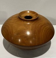 Front angled view of warm tone wood turned vessel with subtle sheen, showing rounded bulbous shape with small flared opening at top.