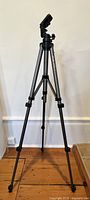 Full view of professional camera tripod stand fully extended on wooden floor against a white wall