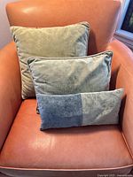 Three green velvet throw cushions in staggered sizes on an orange leather chair, showing overall look and size comparison.