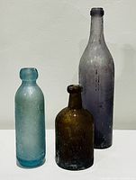 Three tumbled glass bottles with varying heights and colors (purple, blue, amber) shown against plain background, illustrating size and condition.