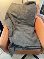 Grey wool blanket casually draped over a brown armchair showing texture and size.