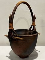 Front view of rounded brown pottery basket with attached arching wooden handle, showing texture and shape.