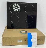 Black glass induction cooktop resting on its original cardboard packaging, user manual and some installation hardware placed in front.