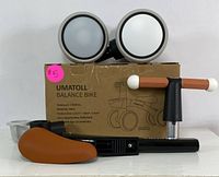 Balance bike parts including two wide grey wheels, brown seat, handlebar with grips, and frame pieces, displayed with the original box.