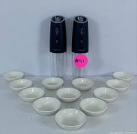 Full view of two electric grinders and fourteen small white ceramic dipping bowls arranged on a white surface.