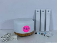 Essential oil diffuser with white power cord and three LED light bars with connectors and plugs laid out on a white surface.