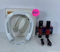 Photo of portable white neck fan with USB cable, two rechargeable black and red LED flashlights with USB charging cables, and background packaging.