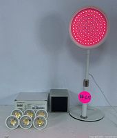 Red light therapy lamp on adjustable stand illuminated with red LEDs in on state, and six LED bulbs with original packaging.