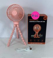 Pink handheld stroller fan with flexible tripod legs, USB charging cable, and original box showing product details.