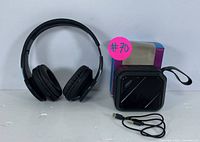 Photo showing black wireless headphones and compact black Bluetooth speaker with charging cable