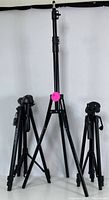 Three black adjustable tripods shown at full height with legs extended, highlighting their sturdy build and various height settings.