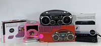 Photo shows black Bluetooth CD boombox, black DVD player with USB port, pink manual kitchen gadget with crank, and two boxed Proscan 7-minute kitchen timers (white and black). All items placed against white backdrop.