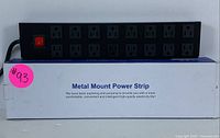 Front view of the power strip placed on its product box showing 12 power outlets and an on/off switch.