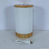 Front view of the rechargeable LED lantern with bamboo top and bottom edges, white diffused body, and USB cable placed in front.