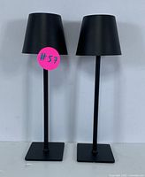 Two black modern table lamps with conical shades and square bases side by side