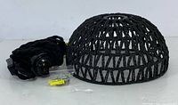 Front view of black woven dome pendant light, long black braided cord coiled beside it, and bagged installation hardware with wall anchors and screws.