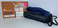 Front view of Angelpet Pet Heating Pad folded with power cord, soft plush dark cover, and orange box packaging showing product info and size.