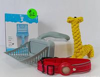 Blue and gray litter scoop, red AirTag-compatible pet collar, and yellow braided rope giraffe toy shown together on a white surface.
