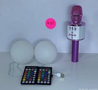 Photo showing purple wireless karaoke microphone, two white spherical RGB lamps, two remote controllers, and USB charging cable