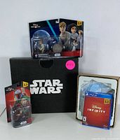 Photo showing PS4 game, Disney Infinity interactive base in plastic, Luke Skywalker and Princess Leia figures packaged together, Boba Fett figure separately, and a Star Wars branded black box