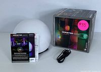 Monster Smart IlluminEssence LED orb light with original packaging, power cable, and instruction manuals displayed on white background.