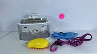 Photo showing entire set with pet water fountain, yellow grooming brush, purple adjustable collar, and blue pet bandana all placed on white surface