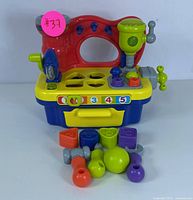 Front view of colorful plastic kids workbench with various colorful tools and shape sorter pieces around it.