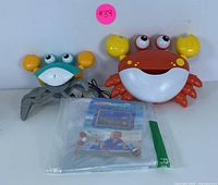 Two musical bubble crab bath toys, one red and one teal, positioned side by side with a packaged instruction manual