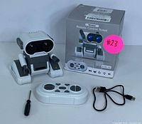 White and gray smart robot with LED eyes, wireless controller, black USB charging cable, small screwdriver, and original box with pink sticker numbering.