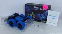 Blue Qunreda remote control stunt car, original box, user manual, and USB charging cable displayed together on a white surface against a white wall.