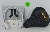 White rechargeable bladeless neck fan displayed with its original packaging and USB charging cable, alongside a black DAWAY bike seat cushion with yellow DAWAY branding on it.