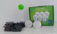 Photo showing the 6-pack green box of full-spectrum LED grow light bulbs with two bulbs outside the box and string lights with black wires.