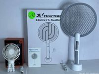 Overview of rechargeable electric fly swatter, its box, stand, USB cable, small portable desk fan with flexible legs, and its charging cable.