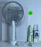Electric fly swatter standing on charging base, with USB charging cable and box behind it, showing brand TMACTIME