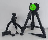 Photo shows larger adjustable tripod with sturdy legs and tilt head alongside flexible mini tripod with segmented articulated legs. Two smartphone mounts and remote shutter control are placed in front.
