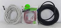 A photo showing a white Ethernet cable, a red USB extension cable still in packaging, and a roll of black speaker wire.