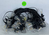 Coiled black wire string lights with multiple clear vintage-style LED bulbs visible, suitable for outdoor use.