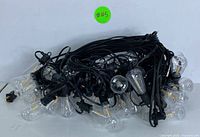 Two coiled and bundled outdoor string lights featuring multiple clear vintage-style Edison LED bulbs on black weatherproof cords with plugs and connectors.