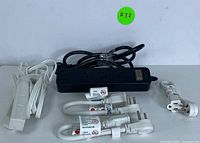 Photo showing one black power strip with three outlets and three USB ports and multiple white extension cords, coiled and labeled.