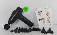 Black handheld rechargeable deep tissue massage gun with seven different detachable massage heads and user manual laid out on white surface.