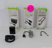 Lot showing three DigiPower boxes: small USB dual-port wall charger, charge and sync cable for iPhone/iPad, and Lightning adapter cable with headphone jack. Below boxes are loose cables and adapters.