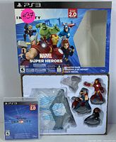 Photo showing the Disney Infinity 2.0 Marvel Super Heroes box with artwork and text. Game disc and five character figures (Iron Man, Thor, Hulk, Captain America, Black Widow) positioned below, some still in plastic packaging.