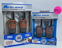 Front view of two Midland X-Talker two-way radio sets in original packaging, one orange/black, one red/black, showing radios and packaging details.